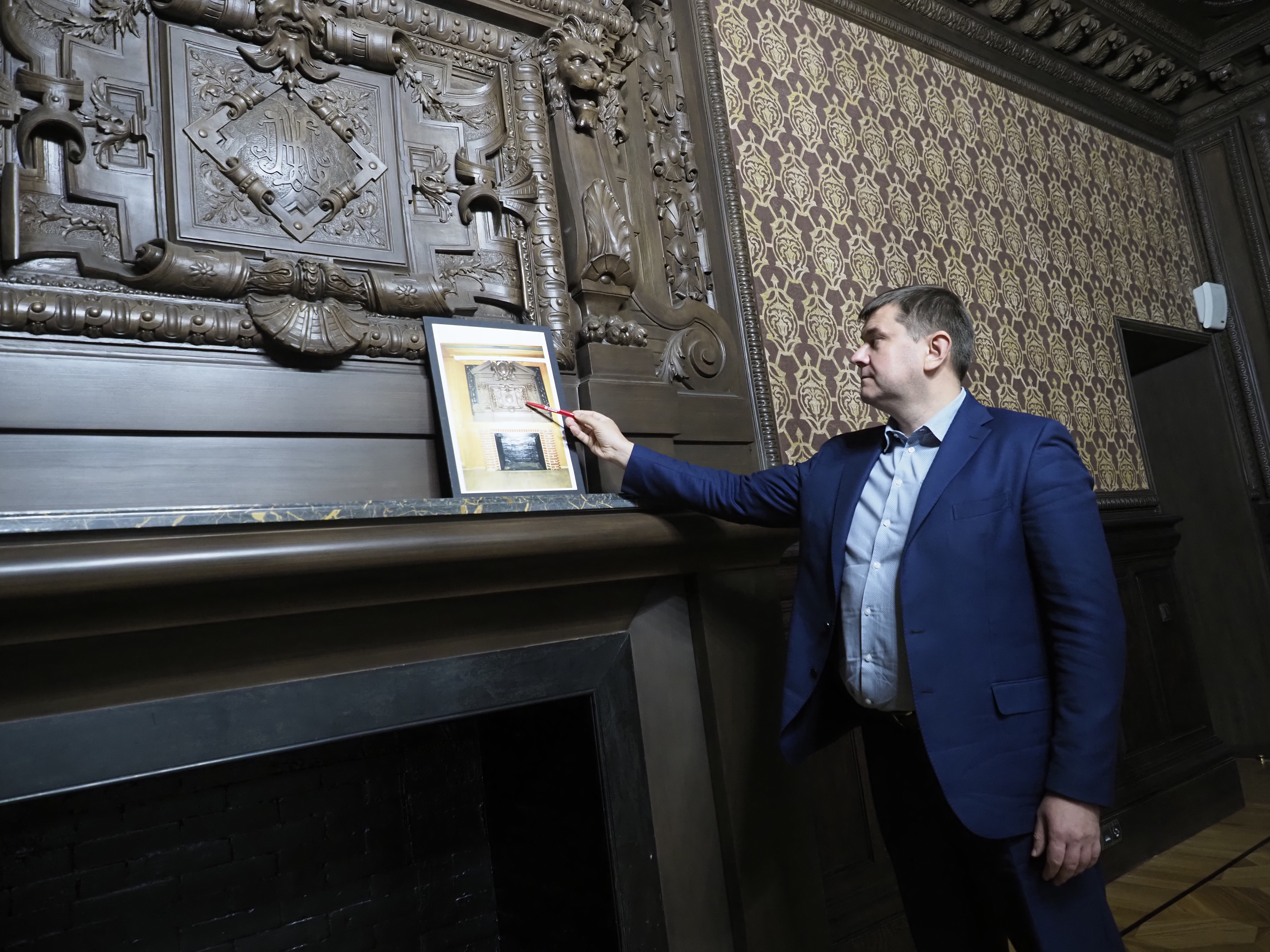 Глава Мосгорнаследия Алексей Емельянов показывает фотографию, на которой видно, как выглядел один из каминов дома до того, как его отреставрировали