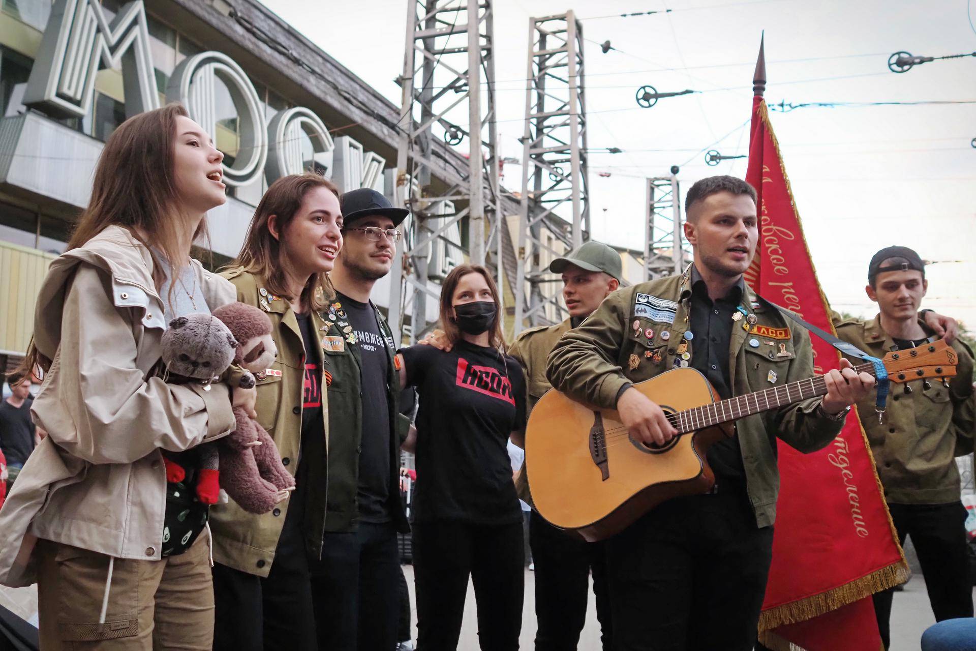 Участники строительного отряда (слева направо) Анастасия Кабылдаева, Мария Лагутина, Арсений Власов, Наталья Белоглазова, Андрей Карлов и Марат Джатдоев поют под гитару, на которой играет Александр Бондарев (в центре). Анастасия Кабылдаева держит талисманы отряда — игрушки Котю и Маника