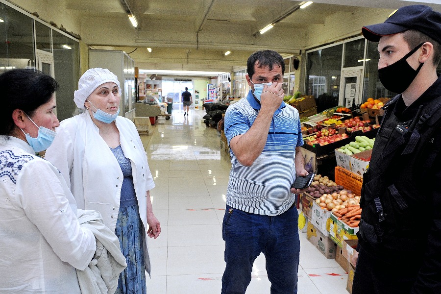 Младший сержант полиции Сергей Ковалев просит продавцов рынка на 33-м километре МКАД Майсори Мамонтурову (слева), Хачиту Эльюергиеву и Джафара Джафарова предъявить документы. У всех троих обнаружены нарушения