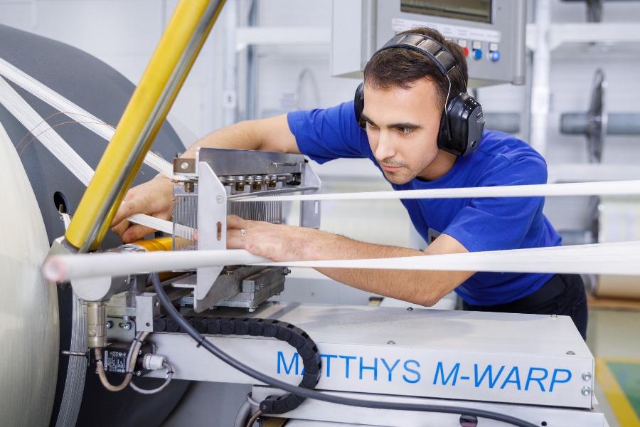 Оператор Иван Подлесный готовит основу для ткацкого станка на производстве средств индивидуальной защиты. У него на голове наушники, которые защищают органы слуха от громкого шума