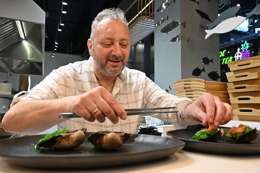 Итальянский шеф-повар Стефано Заффрани готовит морепродукты к подаче на стол: на тарелке раскрыты устрицы, рядом — морские ежи. Гости фуд- молла, где держит три точки общепита итальянец, могут видеть весь процесс приготовления еды