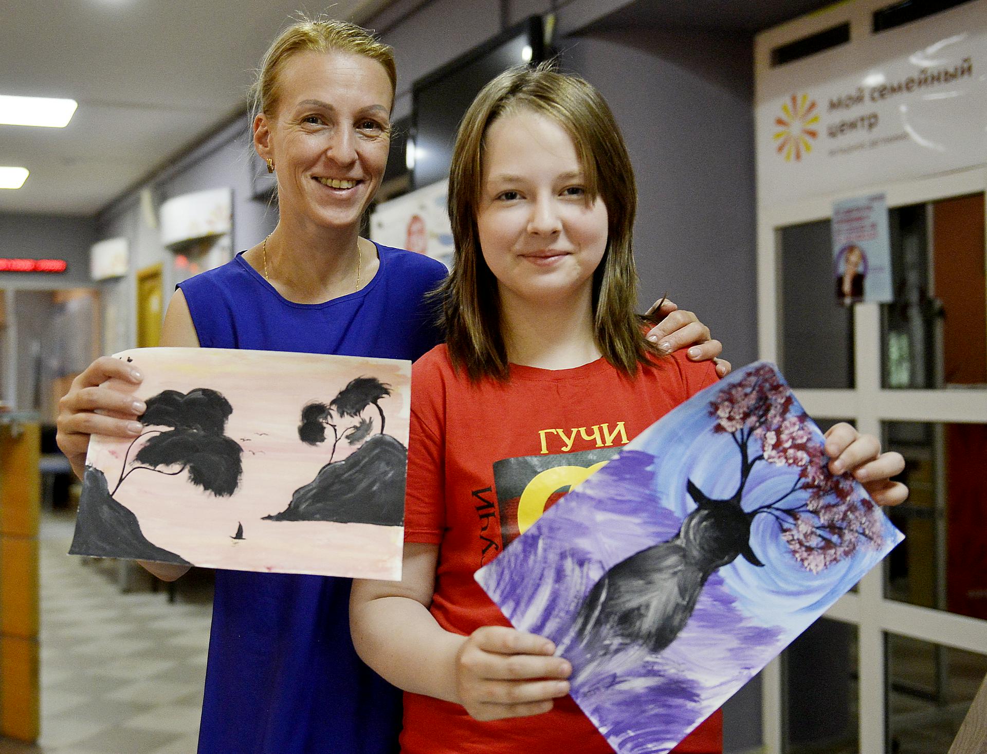 Москвичка Светлана Кузовлева вместе со своей 12-летней дочерью Полиной держат в руках рисунки, которые девочка нарисовала на летних онлайн-занятиях семейного центра «Западное Дегунино»