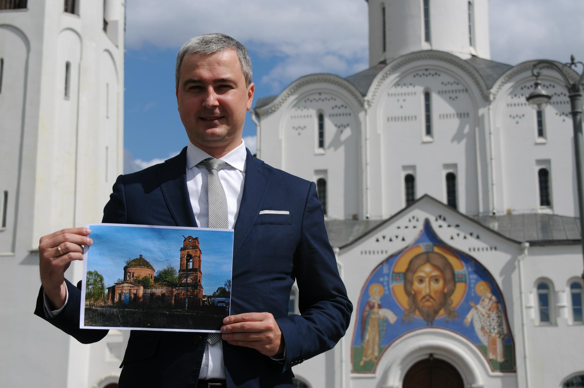 Москвич Павел Осипов позирует на фоне храма Николы Чудотворца у Тверской заставы — мимо этой святыни он ежедневно ходит на работу. В руках у Павла — фото переданного им Белевской епархии храма. Мужчина очень надеется скоро увидеть строение обновленным и готовым принять прихожан