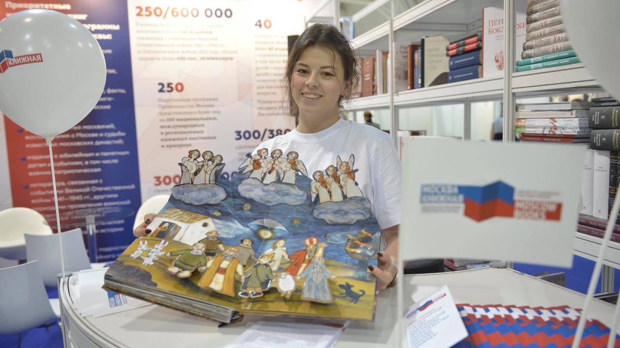 Московская международная книжная ярмарка. Сотрудник стенда Издательской программы правительства Москвы «Москва книжная» Диана Подлипенко демонстрирует книгу для детей о Рождестве
