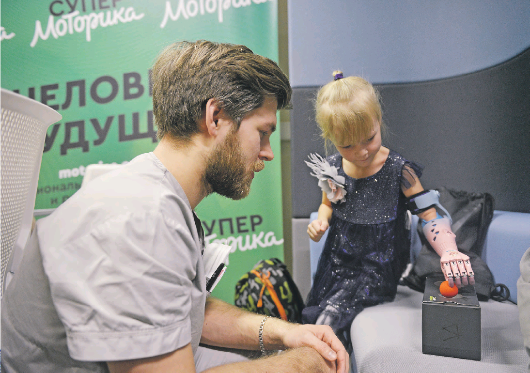 Инженер-протезист Данил Емелин следит, как Анастасия Ананьева выполняет упражнения на мелкую моторику с помощью тягового протеза. Это третье устройство в жизни Насти, и девочка уже мастерски управляется с роборукой