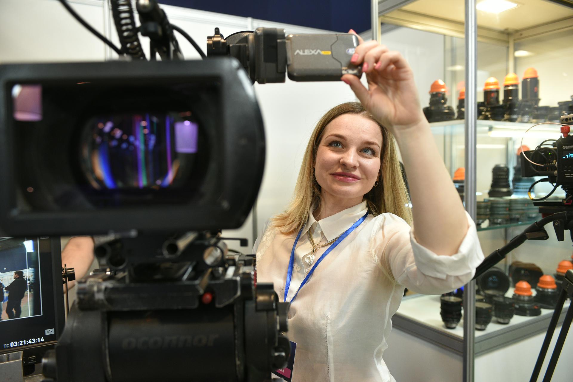 Представительница стенда одной из столичных компаний по производству и аренде оборудования Ирина Павлова рядом с современной камерой. За ее спиной — оптические объективы вековой давности