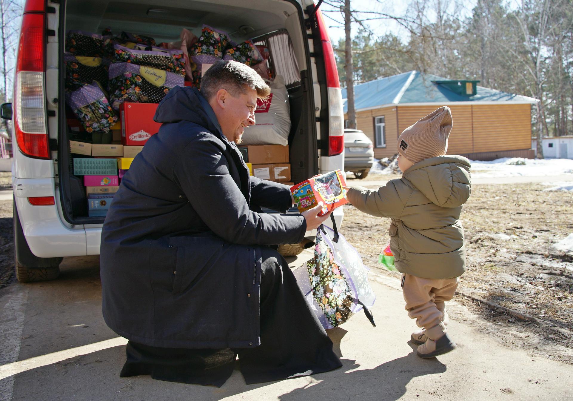 Руководитель молодежного отдела Московской городской епархии протоиерей Кирилл Сладков вручает подарок двухлетнему беженцу Богдану Липовко. Сейчас маленький Богдан живет в Подмосковье вместе с мамой — Натальей Магаляс