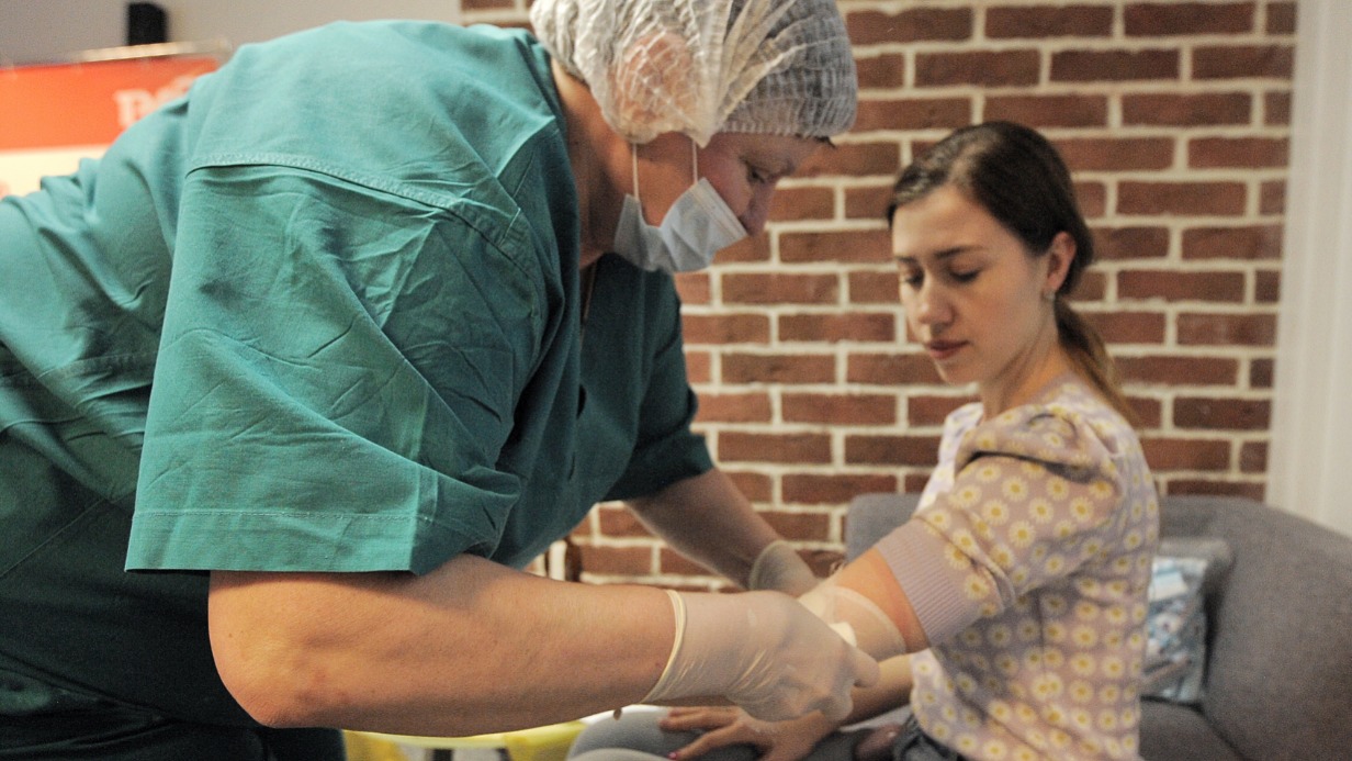 Медсестра Центрального военного клинического госпиталя Валентина Усачева (слева) перевязывает руку донору — специалисту отдела маркетинга РЖД Дарье Мигриной