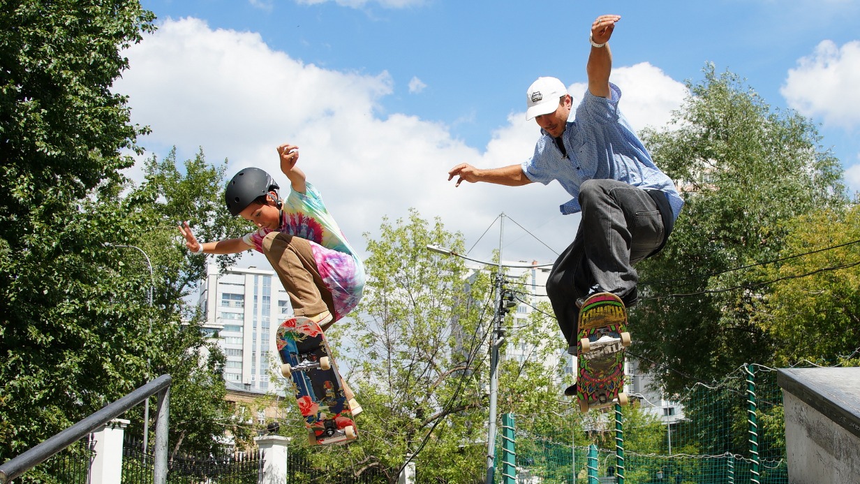 Тренер, первый чемпион России по скейтбордингу Дмитрий Двойнишников и его ученик, десятилетний Степан Литвинов, выполняют совместный трюк на скейтплощадке в парке «Красная Пресня»