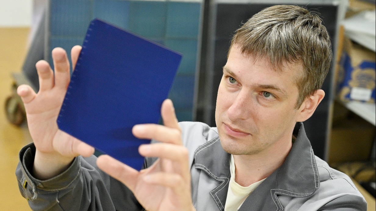 Электромонтажник Александр Голубушин держит в руках элемент солнечной пластины — благодаря поддержке города предприятие, на котором он работает, смогло модернизировать и расширить собственное производство