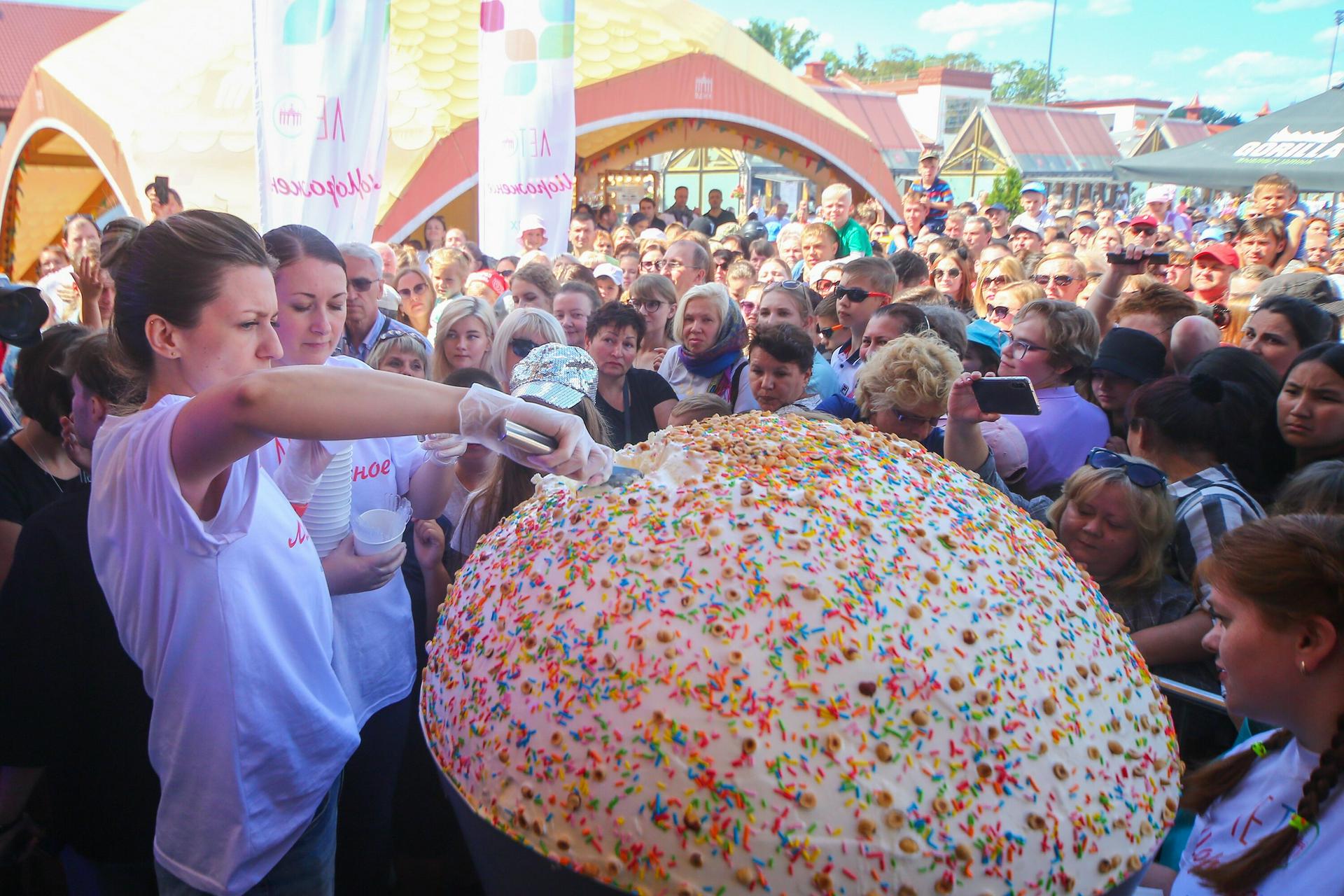 Волонтер Елизавета Морошко (слева на переднем плане) накладывает первую партию рекордного 100-килограммового мороженого, украшенного разноцветной кондитерской посыпкой и орешками, которое приготовили на ВДНХ