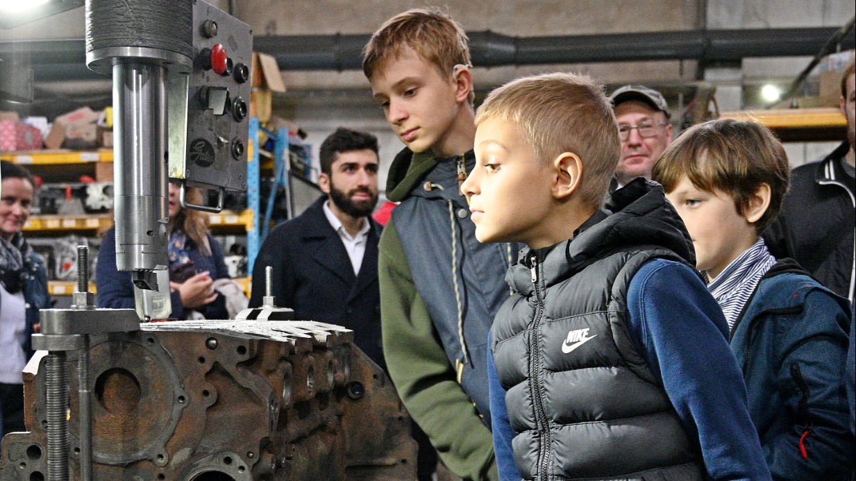 Школьники Захар и Егор Ивановы вместе с Борисом Шпонтаком (слева направо) рассматривают двигатель автомобиля во время экскурсии по заводу, на котором занимаются восстановлением деталей и агрегатов. Посетить предприятие ребята смогли благодаря акции «День без турникетов»