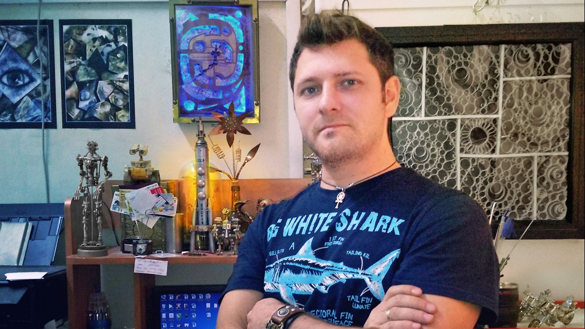 Москвич Виктор Тимофеев у себя в мастерской. Слева за его спиной находится первая поделка — настенные часы