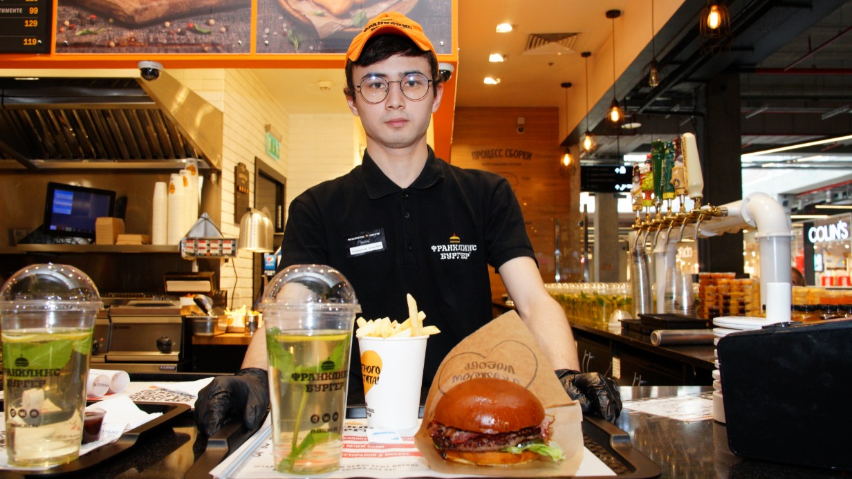 Кассир Диербек Рустамов подает бургер, напиток и картошку и картошку фри в одном из столичных общепитов  