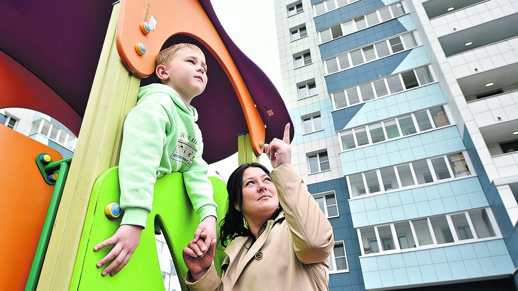 Москвичка Анастасия Азарова показывает сыну Никите Азарову, осваивающему детские горки во дворе дома, построенного по программе реновации, на каком этаже они живут