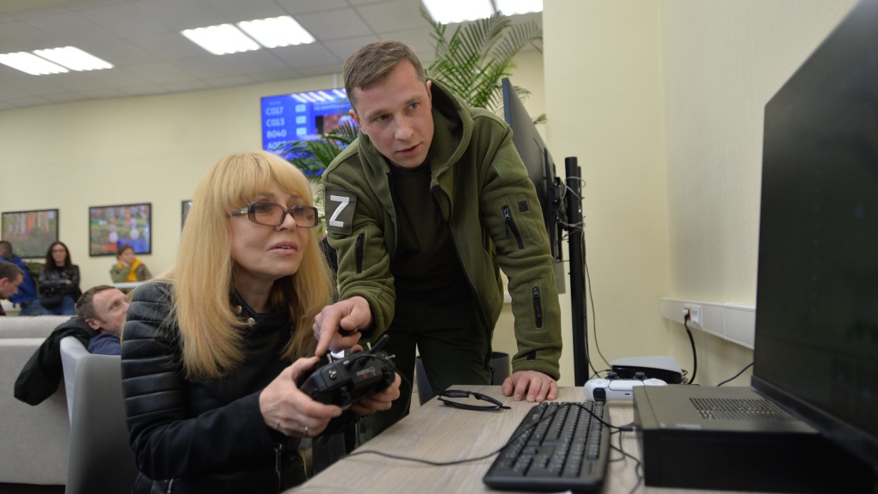 Специалист пункта отбора на военную службу по контракту показывает певице Ольге Кормухиной, как управлять виртуальным дроном