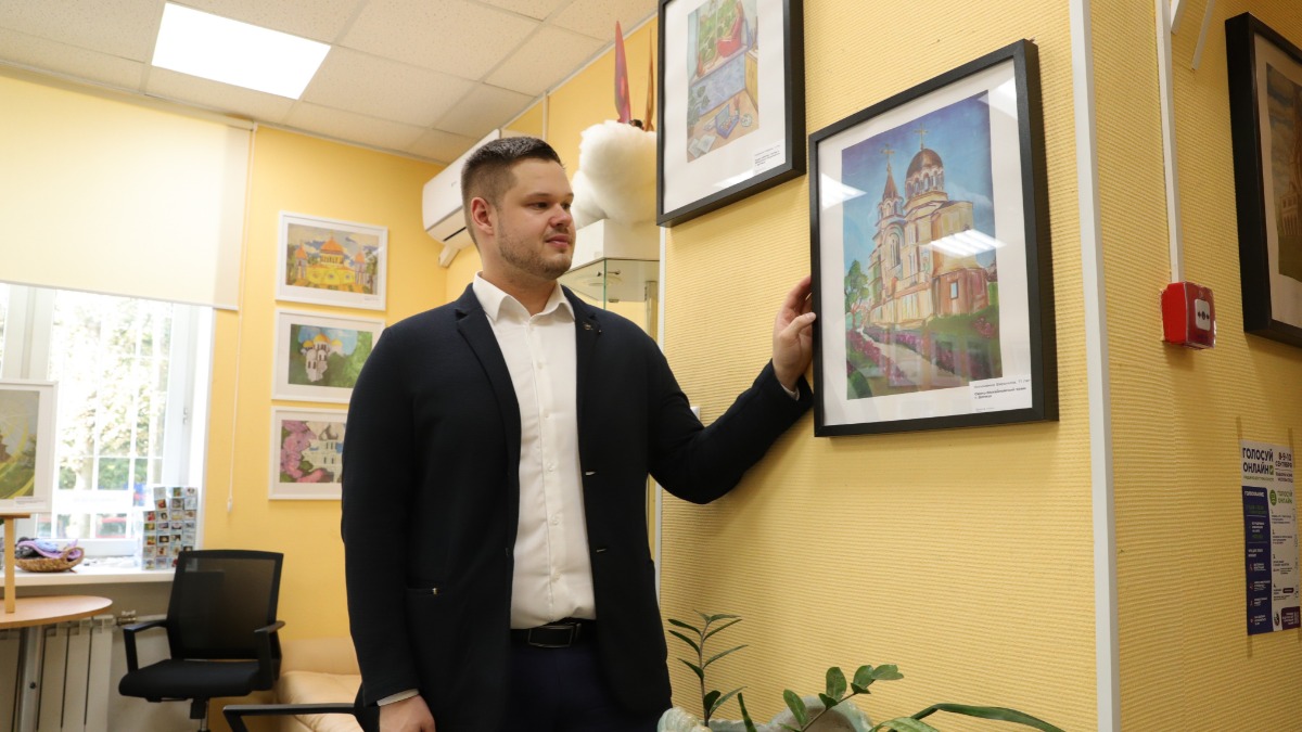 Заместитель руководителя представительства ДНР в Москве Владислав Никитюк смотрит на рисунок 11-летней жительницы республики Вероники Устименко