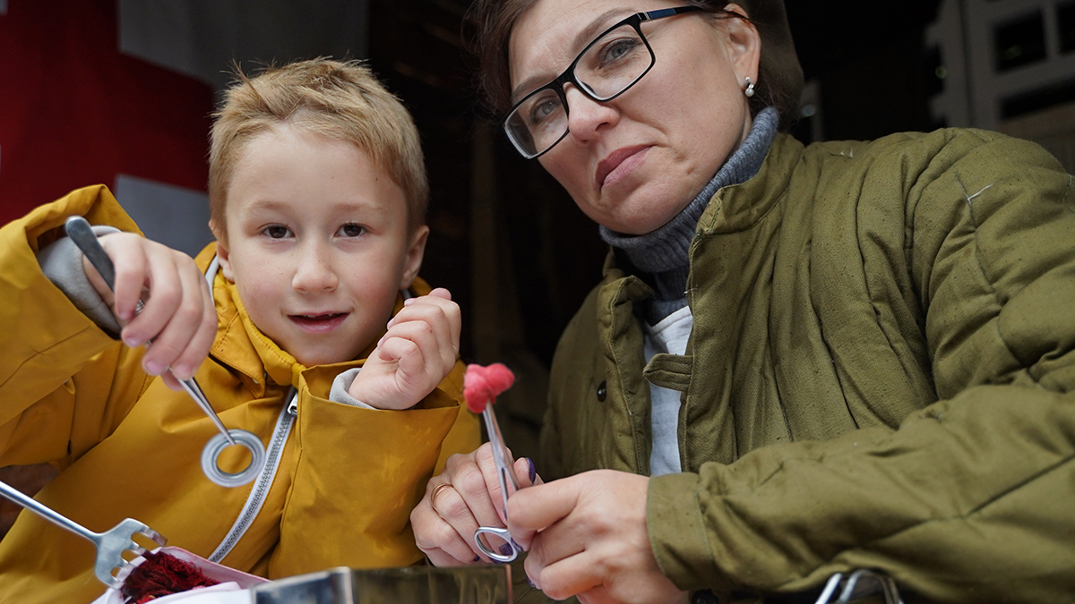 Реконструктор Анжелика Асютина учит юного Акима Кулешова доставать осколки из раны. Мальчик тренируется на кусочке марли, из которой он аккуратно вытаскивает пинцетом металлические монетки