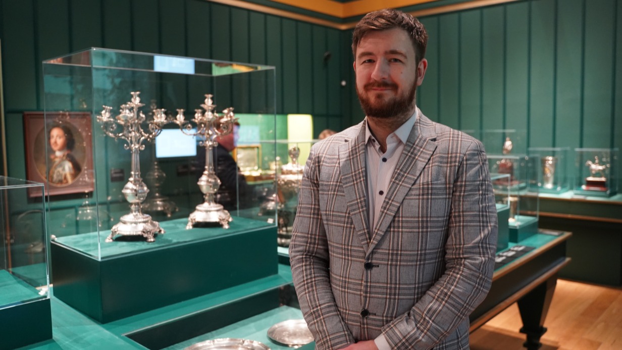 Куратор выставки «Сокровища полковых музеев» в Государственном историческом музее Сергей Сергушкин рассказал о старинных реликвиях полковых музеев России XIX–XX веков. На стенде позади него — серебряные предметы, которые раньше дарили полкам в честь различных событий