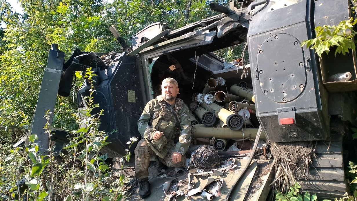 Замполит добровольческого отряда с позывным «Знак» на фоне подбитого «Бредли»