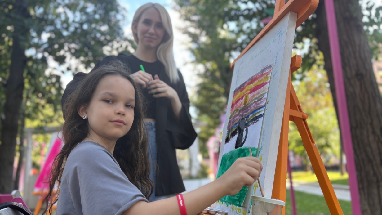 Юная участница мастер-класса на Тверском бульваре Кира Суслова рисует котенка и радугу. Помогает ей педагог Екатерина Мельничук