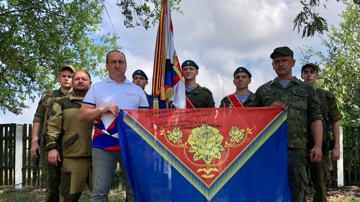 Руководитель АНО «Союз» Павел Тюляев и военнослужащие 110-й бригады Вооруженных сил РФ в Донецкой Народной Республике. Представитель волонтерской организации и офицер подразделения держат флаг Павлово-Посадского городского округа с подписями и пожеланиями