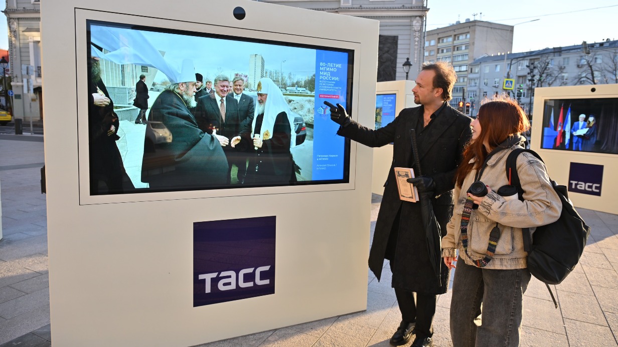 Антон Веселов и Ксения Реброва рассматривают фотографии на медиаэкранах, установленных на благоустроенной площади перед зданием ТАСС