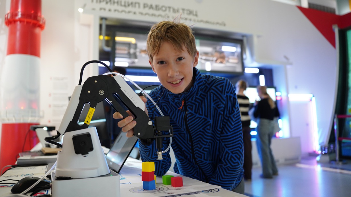 Участник интенсива «Инженерные каникулы» Александр Прокофьев с уменьшенной учебной версией роботизированной руки, которая запрограммирована на перемещение кубиков на разные места