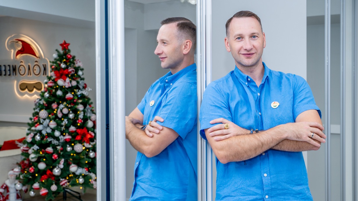 Основатель Фабрики новогоднего настроения Николай Коломеев на фоне ели с украшениями ручной работы