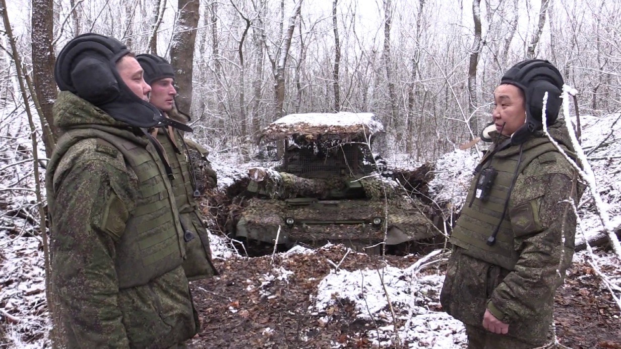 Командир экипажа танка группировки войск «Восток» «Банхарт» (справа) поручает боевое задание механику-водителю «Аргуну» (слева на переднем плане) и наводчику-оператору «Богомолу»