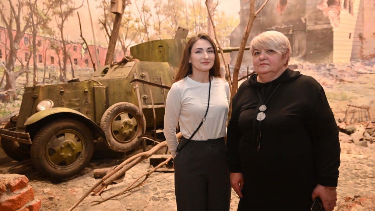 Экскурсовод Ксения Даньшина и заведующая отделом «Центр экскурсионного обслуживания» Музея Победы Елена Наумова показывают посетителям часть выставки «Подвиг Народа», оформленной в виде двора цитадели Брестской крепости во время Великой Отечественной войны