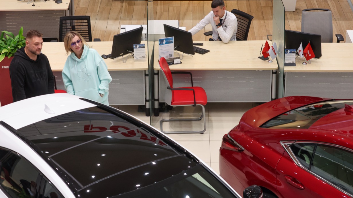 Посетители автомобильного салона выбирают подходящую машину с пробегом