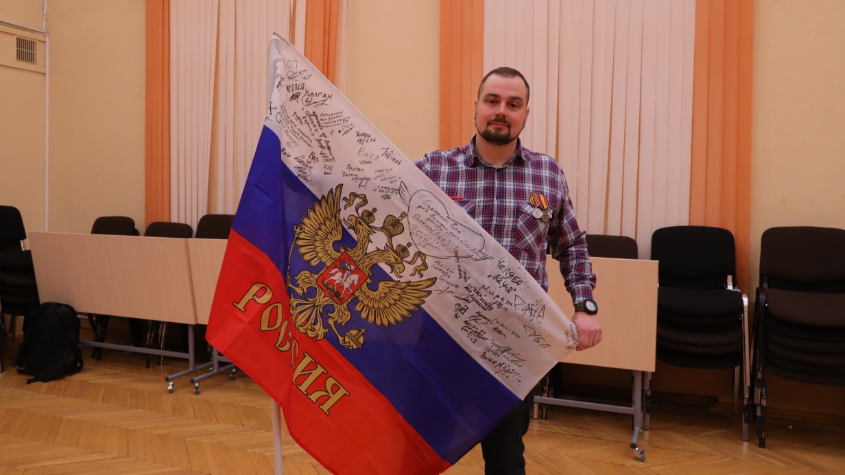 Участник специальной военной операции с позывным «Бур» держит в руках российский триколор, расписанный бойцами мотострелкового полка