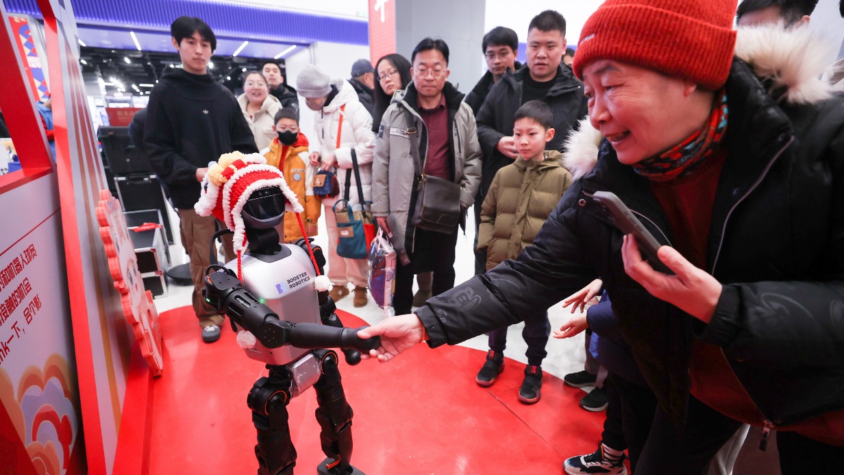 Посетительница ярмарки храма науки и технологий Весеннего фестиваля в Пекине (Китай) пожимает руку роботу в праздничной шляпе