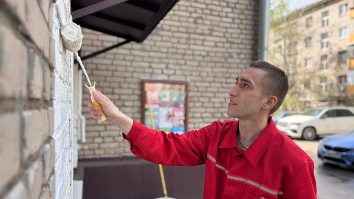 Дворник Владислав Паламарчук красит часть фасада у подъезда