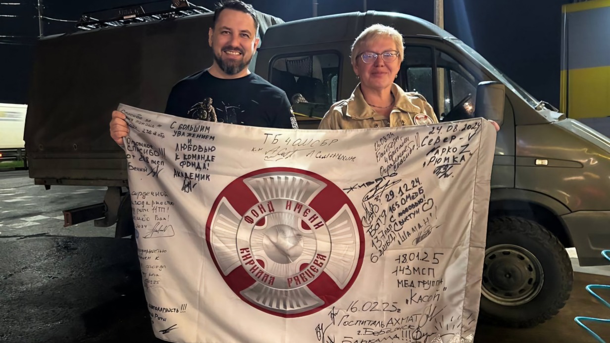 Основатель Фонда имени Кирилла Рябцева Светлана Рябцева и волонтер Александр Когтев держат флаг с пожеланиями от врачей и российских бойцов