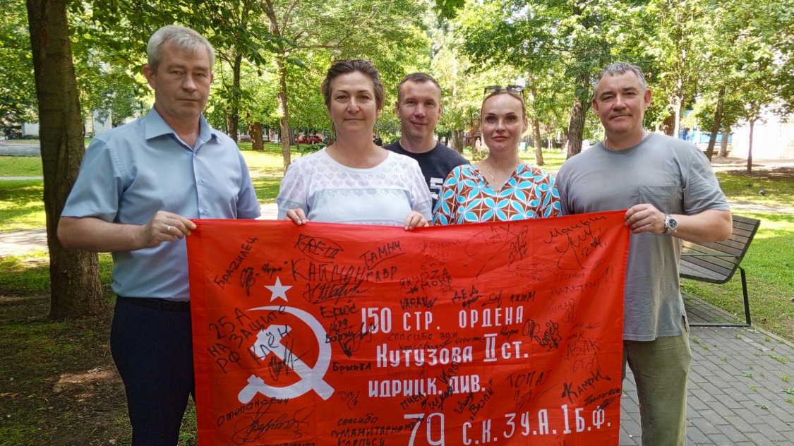 Командир 2-го батальона 1429-го мотострелкового полка Юрий с позывным «Волк» и члены волонтерского корпуса Татьяна Данилочкина, Дмитрий Сырцев, Наталья Мельникова и Денис Балуев держат флаг с автографами военнослужащих