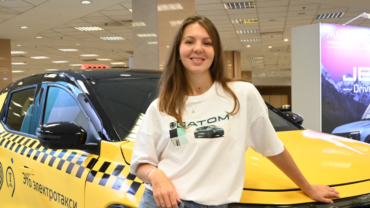 Представитель PR-отдела компании АО «Кама» Елена Роговая показывает участникам XIII Международного Евразийского форума «Такси» новый российский электромобиль «Атом», который представлен в версии для такси