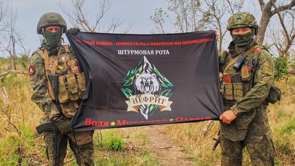 Офицер, командир роты штурмовиков 36-й армии с позывным «Инструктор» и командир взвода огневой поддержки «Приморец» несут боевое знамя их подразделения