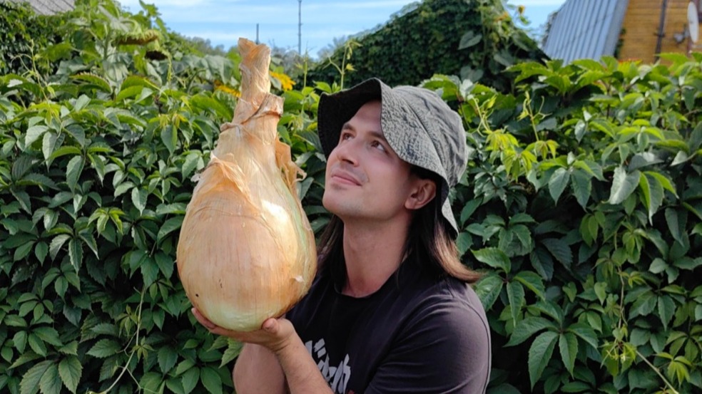 Садовод Александр Чусов держит в руках луковицу