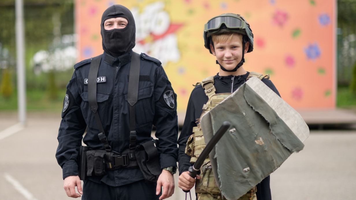 Сотрудник ОМОН «Авангард» столичного главка Росгвардии Кирилл помогает участнику городского клуба «Лето Побед» Дмитрию Андрианову почувствовать себя настоящим спецназовцем