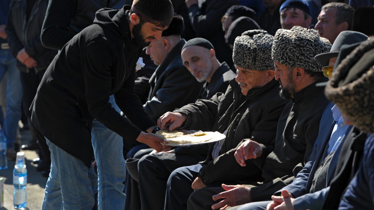 Молодой человек угощает старших чапильгом — лепешками с начинкой из творога и зелени, смазанных сливочным маслом