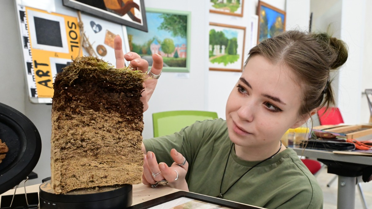 Аспирантка факультета почвоведения МГУ Мария Чепурнова показывает посетителям выставки почвенный профиль, похожий на слоеный торт
