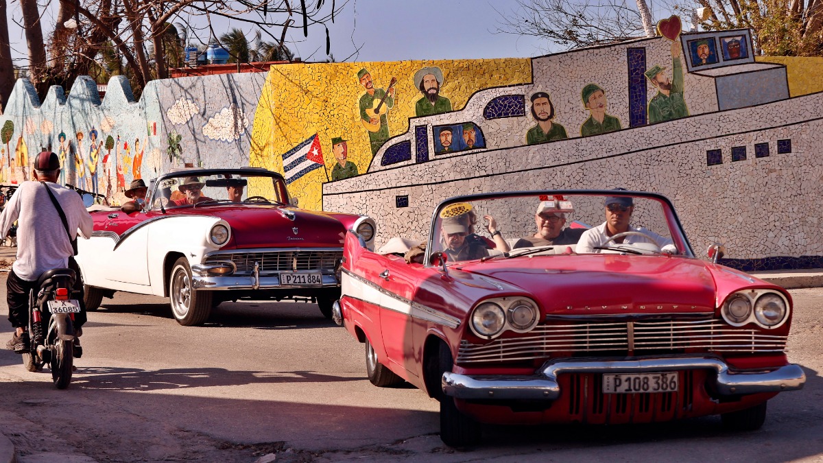 Туристы едут на классических автомобилях, проезжая перед фреской художника Хосе Фустера в рыбацком городке Хайманитас на окраине Гаваны (Куба)