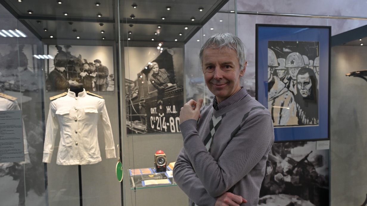 Куратор выставки, заведующий экспозиционно-выставочным отделом Государственного музея обороны Москвы Олег Кржижановский на фоне стенда, посвященного работе метрополитена и железных дорог. В витрине — белый китель сотрудника московского метро образца 1943 года