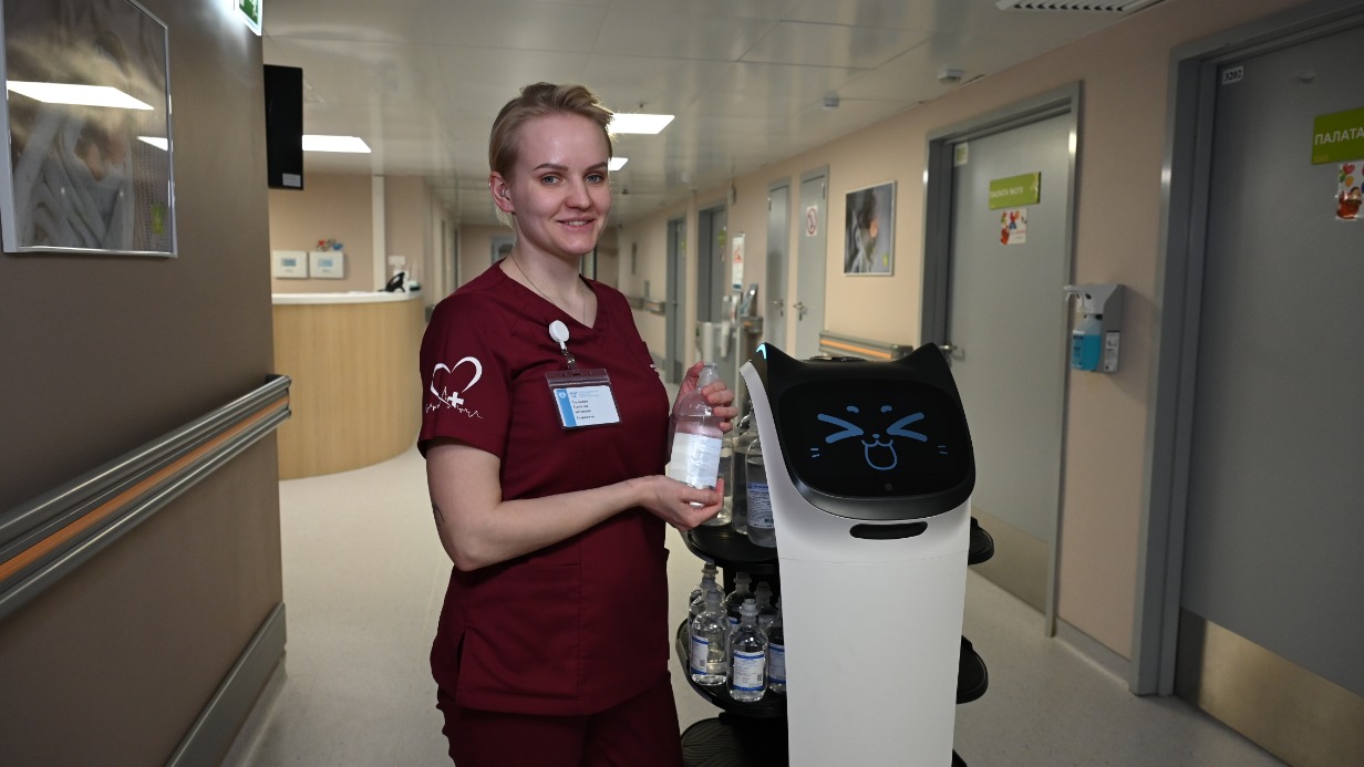 Старшая сестра отделения реанимации и интенсивной терапии новорожденных ГКБ № 67 Наталья Талькова нагружает робокошку бутылочками с физраствором — роботы помогают медикам выполнять рутинные задачи